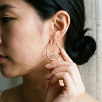 Thumbnail for Custom Name Hoop Earrings in Rose Gold held between the fingertips, scale reference | SKU: name-hoop-rose-gold-30-mm