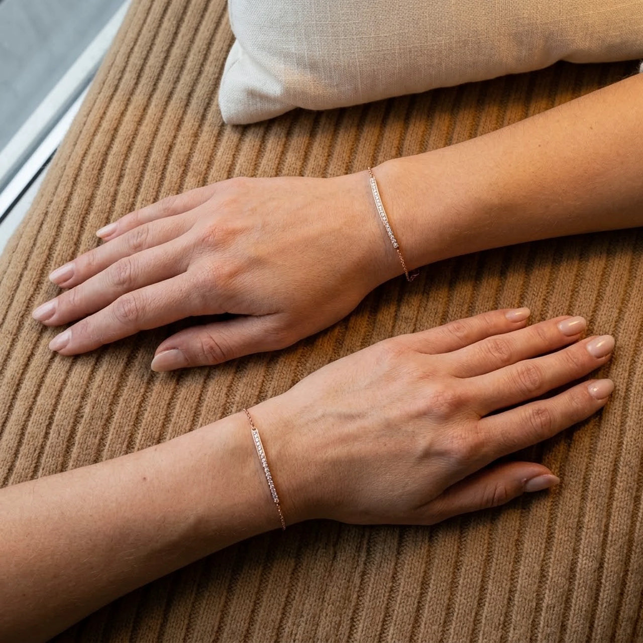 Two wrists wearing the rose gold Crystal Bar Bracelet, seen from above on camel wool